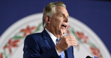 Former Virginia Governor Terry McAuliffe in a dark suit gesturing as he speaks at a podium with the seal of Virginia in the background