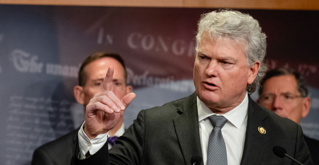 Mike Collins raises his hand in a dramatic pose at a Capitol Hill press conference.