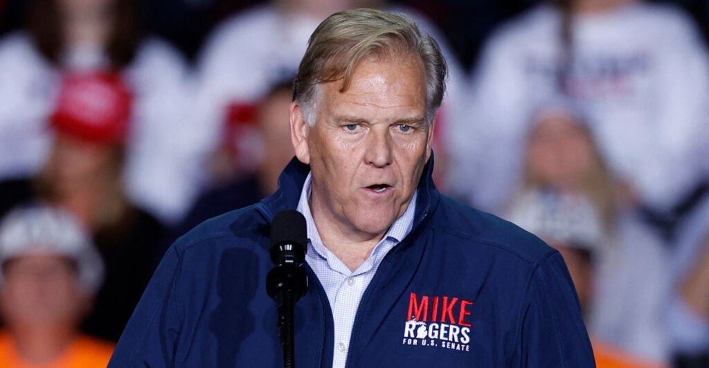 Mike Rogers, dressed in a campaign-branded fleece, speaks at a Trump rally in 2024.