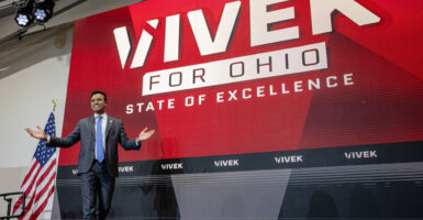 Vivek Ramaswamy gestures to the crowd as he stands in front of a billboard from his campaign.