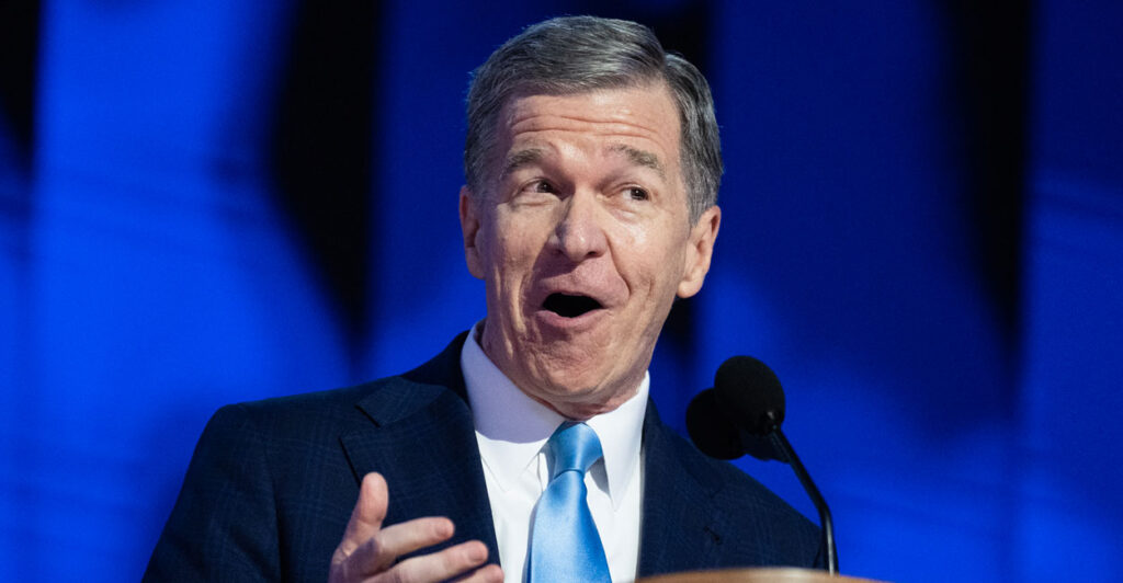 Roy Cooper speaks at a lectern before a Democrat crowd.