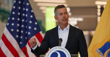 Transportation Secretary Sean Duffy in a suit with no tie gestures with his right hand while speaking at a podium.