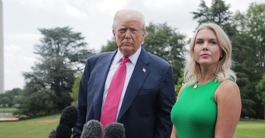 Donald Trump in a blue suit stands next to Karoline Leavitt in a green dress