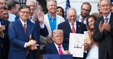 President Donald Trump, wearing a navy suit and red tie, holds up a signed bill while GOP lawmakers applaud
