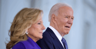 Jill Biden in a purple suit stands in the foreground; in the background, President Joe Biden, wearing a navy suit and tie, squints ahead.