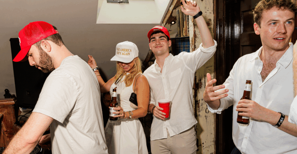 Men and women dressed in white and Make America Great Again hats pose for the camera at a party.