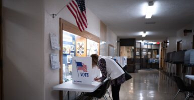 A woman leans over a desk casting her vote.