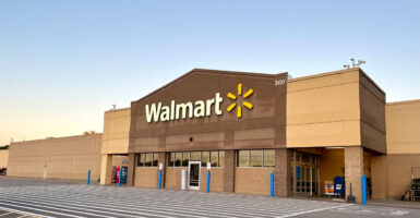 Photo shows the front of a Walmart with a light blue sky behind it.