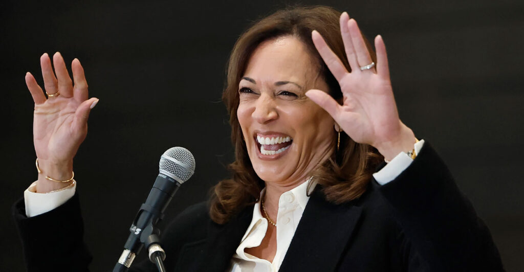 Kamala Harris on stage smiling with both hands in the air