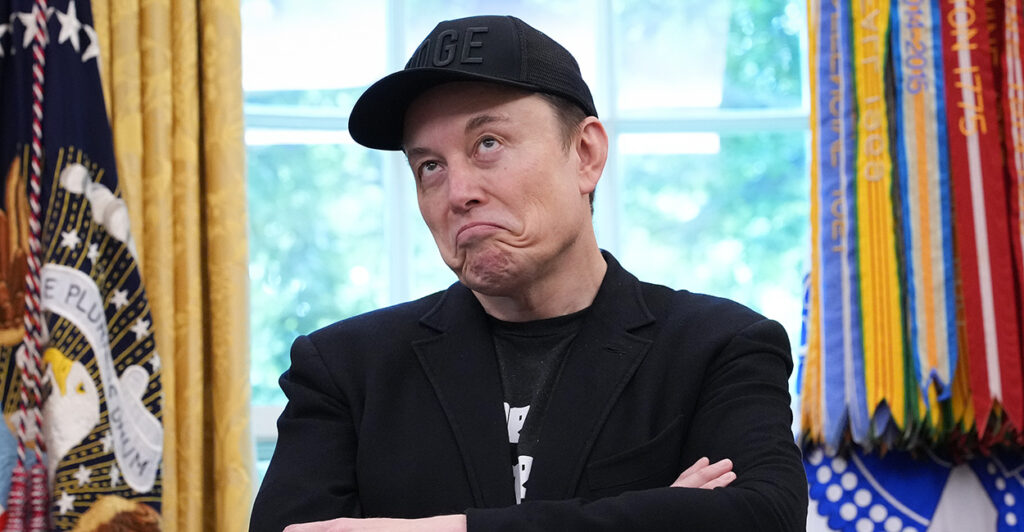 Elon Musk in a black jacket and a black baseball cap in the Oval Office at the White House