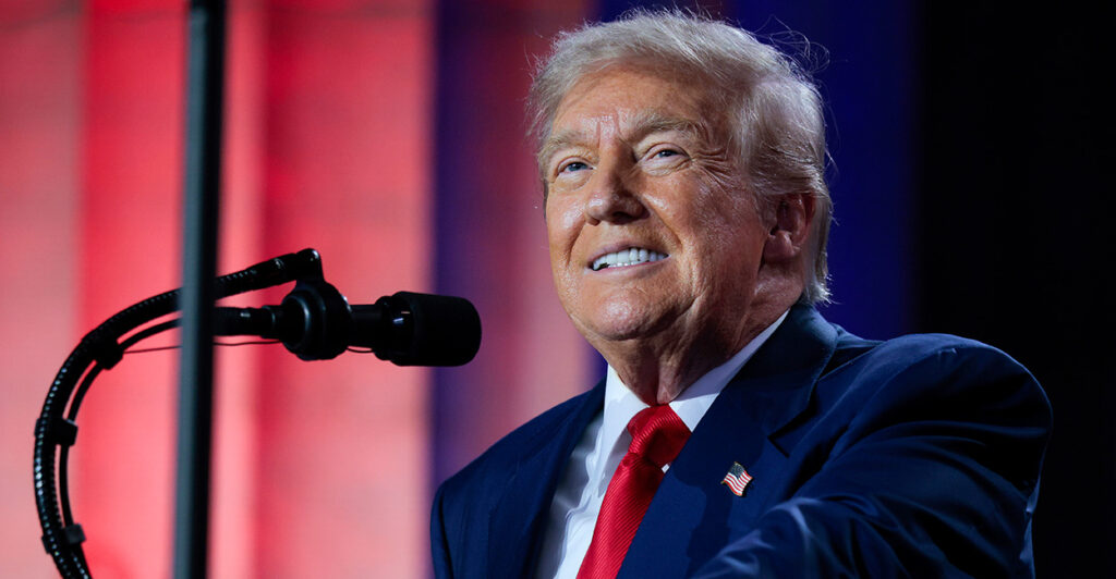 Close-up of a smiling President Donald Trump in a blue suit and red tie.