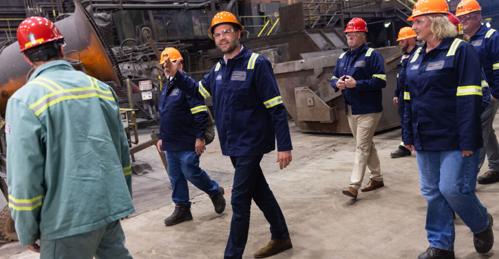 Vice President JD Vance, wearing a hard hat, waves as he tours a factory.