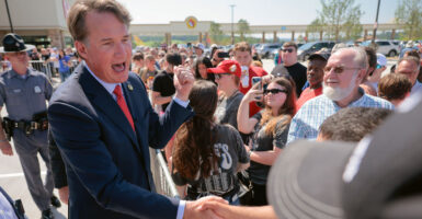 Gov. Glenn Youngkin shakes hands with supporters outdoors and is surrounded by w large crowd.