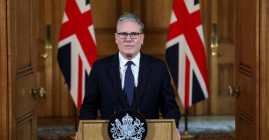 Keir Starmer stands behind a podium and looks straight ahead with two British flags behind him.