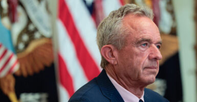 Robert F. Kennedy Jr. sits at a desk during a news conference and stares straight ahead.