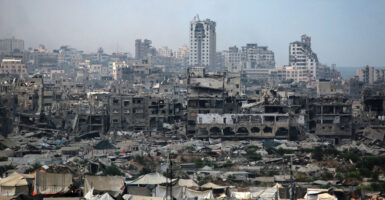 The war torn skyline of Gaza City is shown with tents set up beneath crumbling buildings.