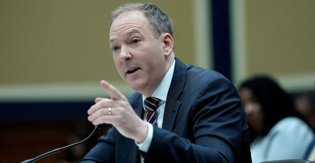 Lee Zeldin sits down and speaks into a microphone while gesturing with his left hand.