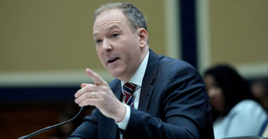 Lee Zeldin sits down and speaks into a microphone while gesturing with his left hand.