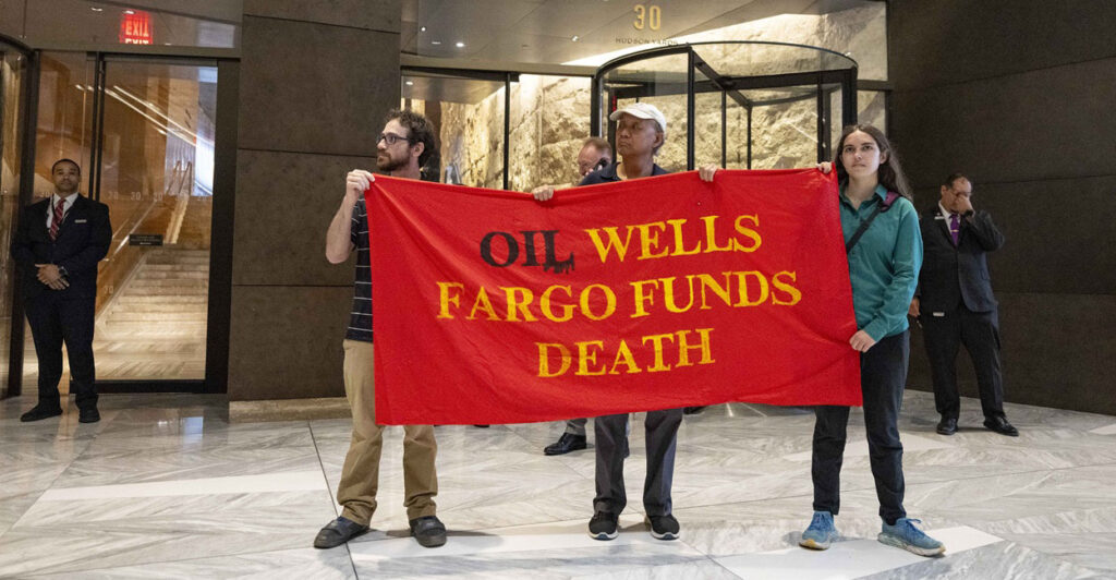 Protesters hold up a sign that says that oil wells and Wells Fargo bank lead to death.