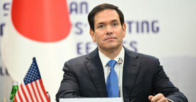 Marco Rubio sits at a table and looks straight ahead with his hands on the table.