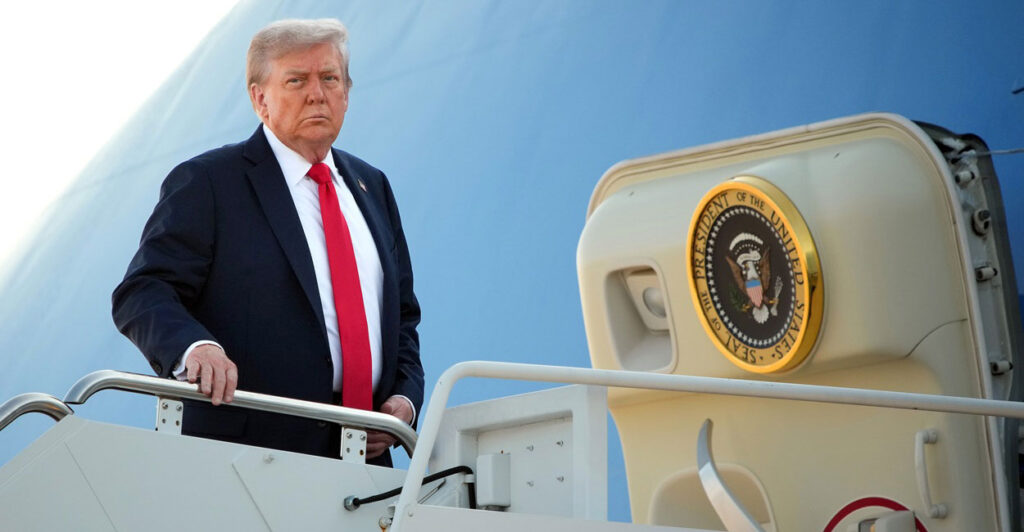 Donald Trump stands on the boarding platform with his right hand touching a rail before he boards Air Force One.