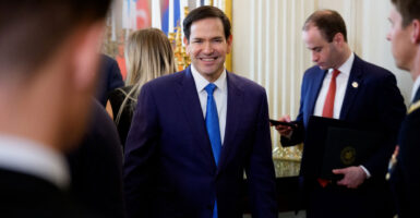 Marco Rubio stands in a room and smiles with his arms by his side.