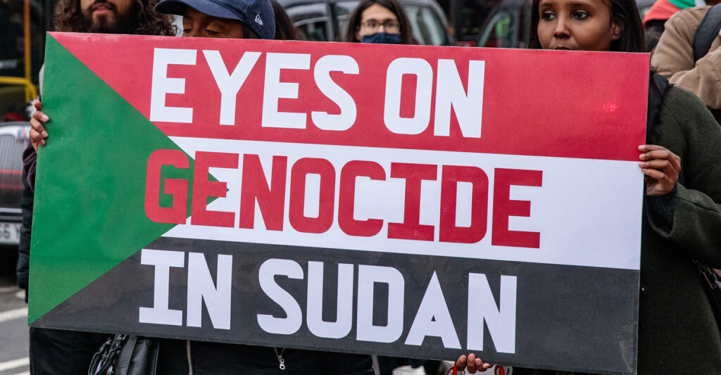 Two people hold up a sign that says, "Eyes on genocide in Sudan."
