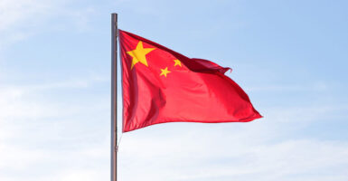 The Chinese flag blows in the wind with blue skies in the background.