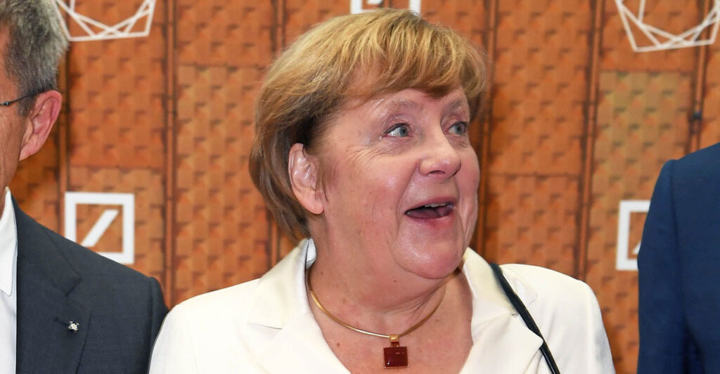Angela Merkel talks while standing on the red carpet and looks to her left.
