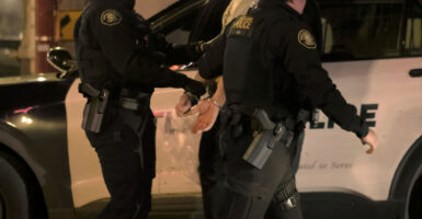 Cops with backs to the camera lead away a suspect.