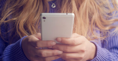 A woman in a purple sweater holds a while cell phone.