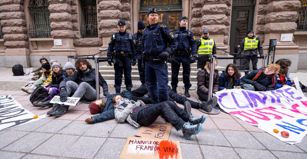 A group of climate protestors sit on the ground, with Greta Thunberg laying on the ground at the feet of several officers.