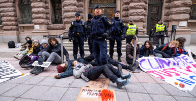 A group of climate protestors sit on the ground, with Greta Thunberg laying on the ground at the feet of several officers.