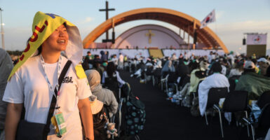 A smiling pilgrim stands at left of frame, as a massive crowd looks toward a stage at the Jubilee of Youth in Rome.