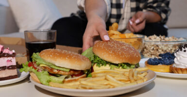 Woman reaches for a burger in the midst of a table of junk food.