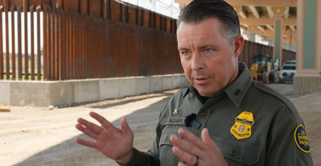 Interim Border Patrol Chief for the El Paso Sector Walter Slosar stands in his green uniform near the border wall.