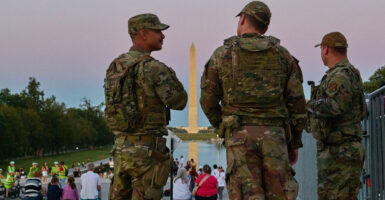 Nearing sunset, three National Guard members look over a group of people gathered on the steps of the Lincoln Memorial, with the Washington Monument in the background.
