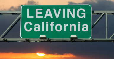 A green highway sign reading "LEAVING California" against the backdrop of the setting sun.