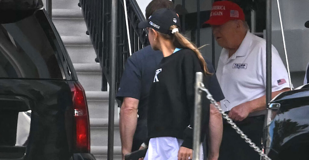 Donald Trump in white golf shirt and red hat prepares to depart for a golf outing with granddaughter Kai as aides and others gather.