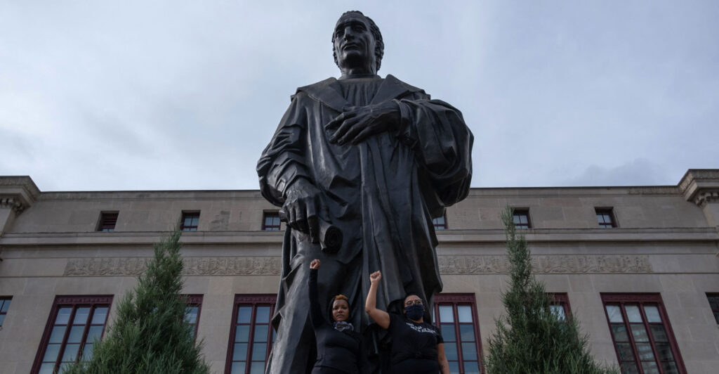 Protesters stand at the Columbus, Ohio statue in Columbus with their fists raised.