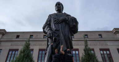 Protesters stand at the Columbus, Ohio statue in Columbus with their fists raised.