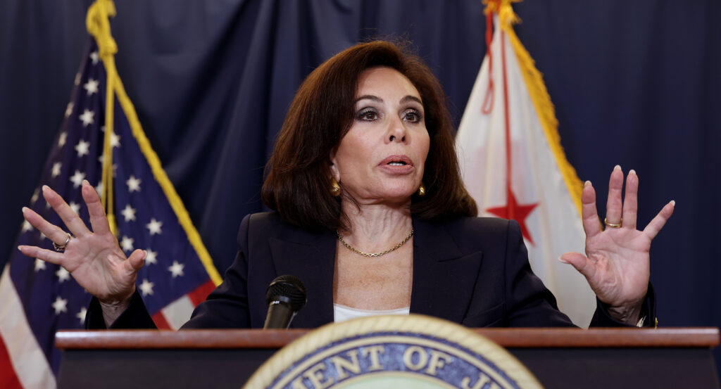 Jeanine Pirro, with her hands raised, stands behind a podium