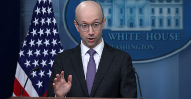 Ian Sams in a dark suit and purple tie stands at the White House press podium speaking to the media