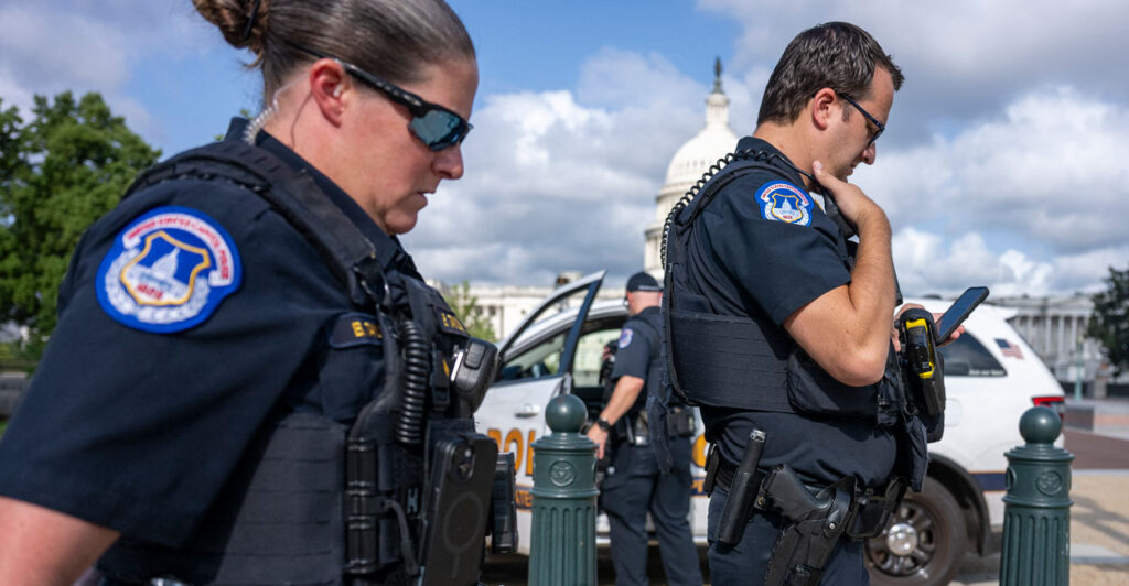 A close up photo shows a male and female U.S. Capitol Police officers walking by in front of the U.S. Capitol.