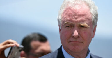 A close-up photo shows Sen. Chris Van Hollen looking on during a press conference.