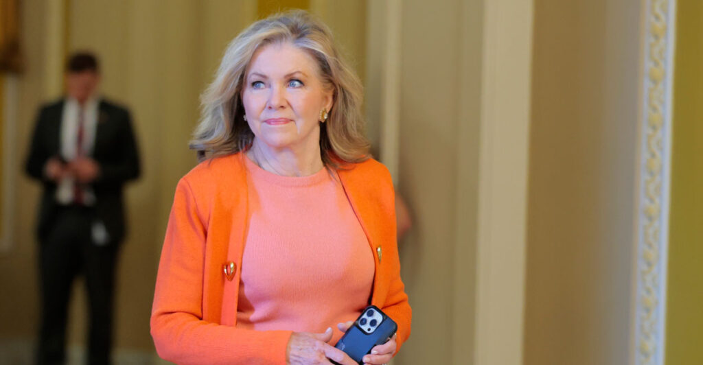 Blackburn walks on the Senate side of the Capitol, dressed in a bright orange sweater.