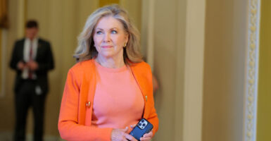 Blackburn walks on the Senate side of the Capitol, dressed in a bright orange sweater.
