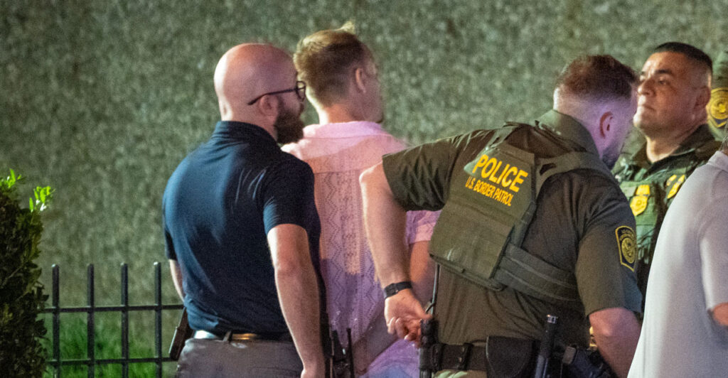 The suspect, a middle aged man in a pink shirt, is handcuffed by officers.