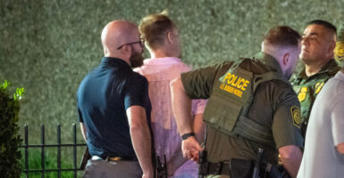 The suspect, a middle aged man in a pink shirt, is handcuffed by officers.