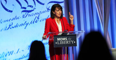 Moms for Liberty CEO Tina Descovich in red behind a banner reading "Moms for Liberty."